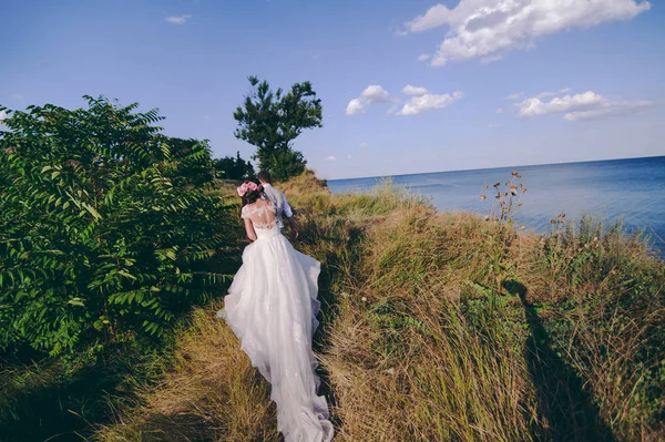 Couple de mariage sur une promenade mariée et marié champ de mer coucher de soleil architecture herbe sable — Photo