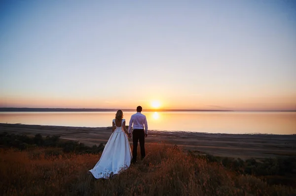 Esküvő házaspár egy sétára menyasszony és a vőlegény tengeri naplemente építészeti fű, homok — Stock Fotó