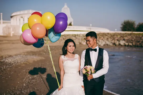 Wedding couple with balls walking along the seashore — Stock Photo, Image