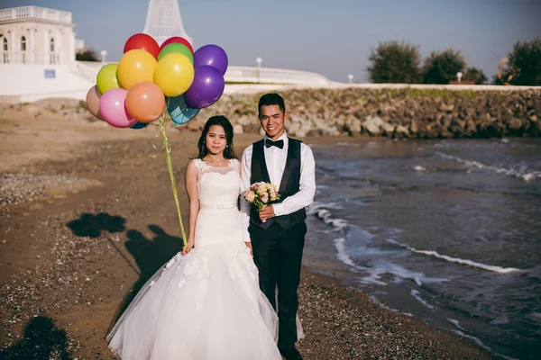 Pareja de bodas con bolas caminando por la orilla del mar —  Fotos de Stock