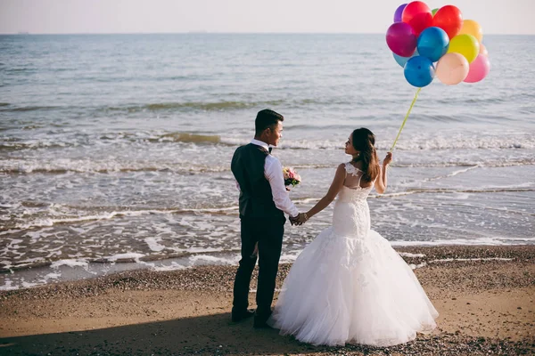 Wedding couple with balls walking along the seashore — Stock Photo, Image
