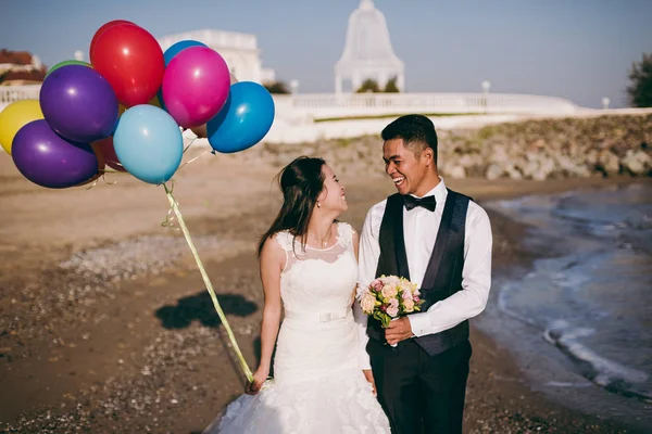Pareja de bodas con bolas caminando por la orilla del mar —  Fotos de Stock