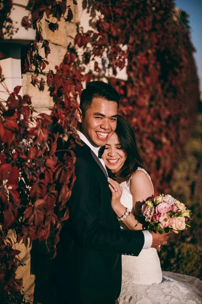 Casamento casal fica perto de uma parede com folhas vermelhas — Fotografia de Stock