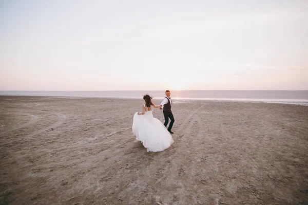 河口の海岸に沿って歩く結婚式のカップル — ストック写真