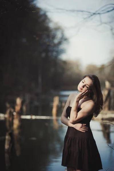 Morena menina fica ao lado da árvore perto da água — Fotografia de Stock