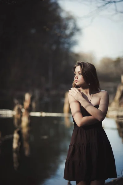 黑发的女孩站在靠近水的地方树 — 图库照片