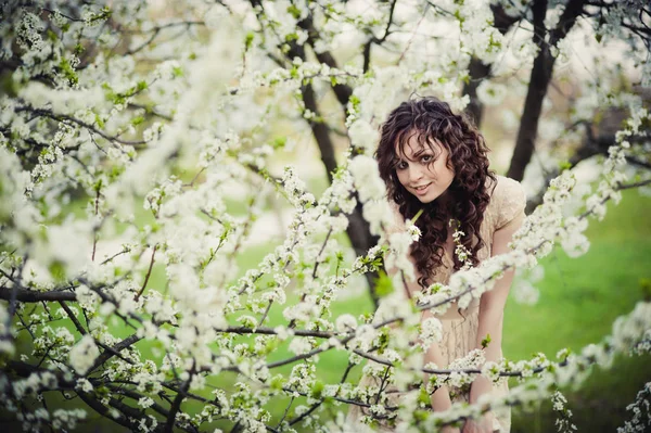 Curly brunette meisje permanent in bloeiende bomen — Stockfoto