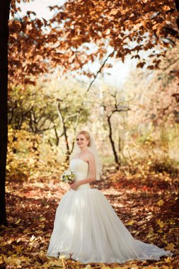 Güneşli bir parkta beyaz elbiseli sarışın gelin