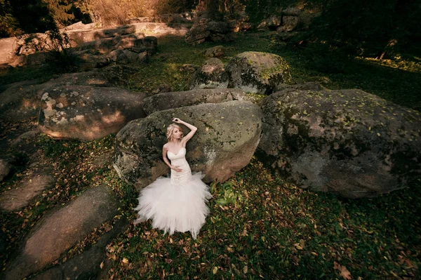 Blond bride in a white dress on a background of large stones — Stock Photo, Image