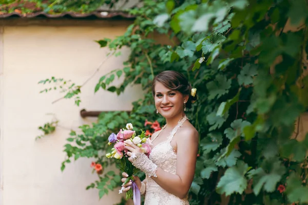 Brunette bride at the wall with weaving leaves — Stock Photo, Image