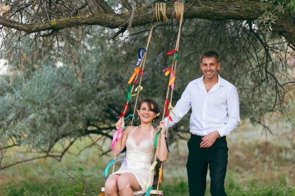 Bruden och brudgummen på en gunga i parken — Stockfoto