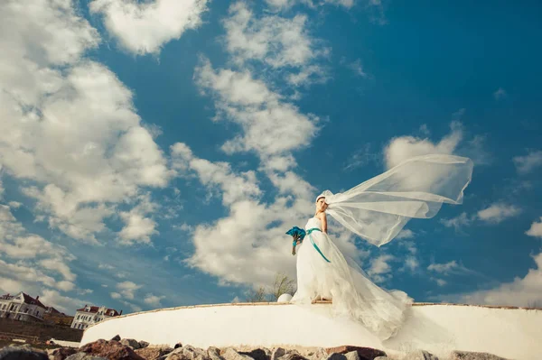 Bride with a long veil for a walk by the sea