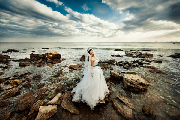Nevěsta s dlouhým závojem na procházku u moře — Stock fotografie