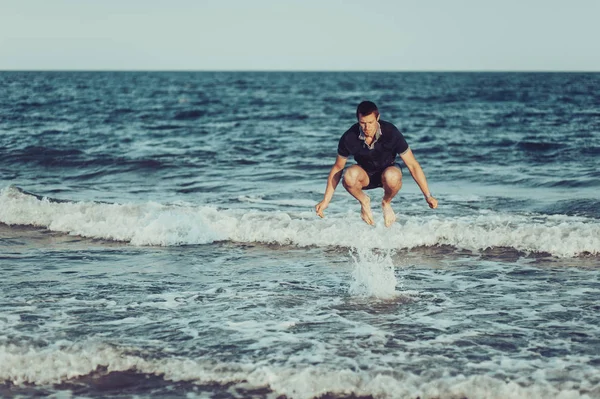Un joven está saltando y divirtiéndose en el mar — Foto de Stock
