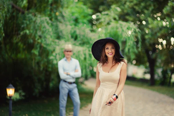 Dívka v klobouku se širokou krempou a člověk na procházce v parku — Stock fotografie