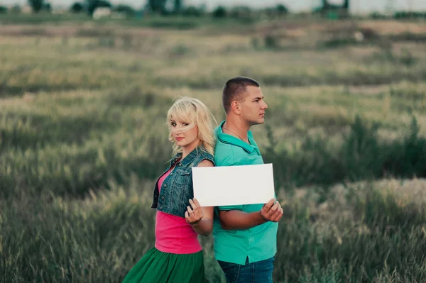 Young couple in love in a tall grass with a white blank sheet — Stock Photo, Image