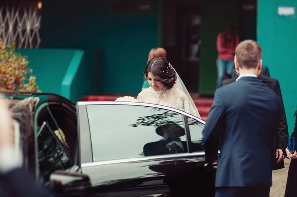 Bride and groom get into a black car — Stock Photo, Image