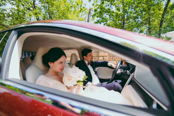 Noiva e noivo estão sentados no salão do carro vermelho — Fotografia de Stock