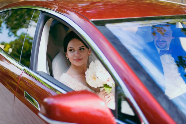 Sposa e sposo sono seduti nel salone di auto rosse — Foto Stock