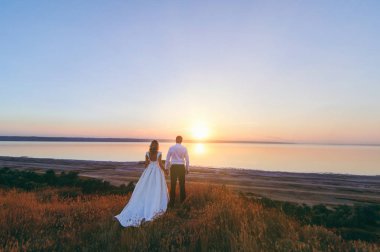 Gelin ve damat birlikte denize yakın gün batımında yürüyor