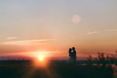 Gelin ve damat birlikte denize yakın gün batımında yürüyor