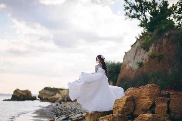 Noiva fica nas rochas perto do mar e nada seu vestido — Fotografia de Stock