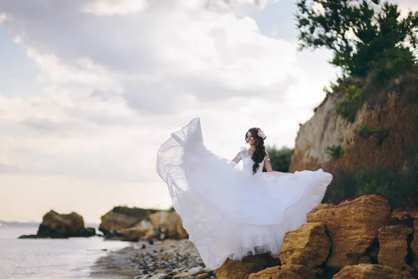 Noiva fica nas rochas perto do mar e nada seu vestido — Fotografia de Stock