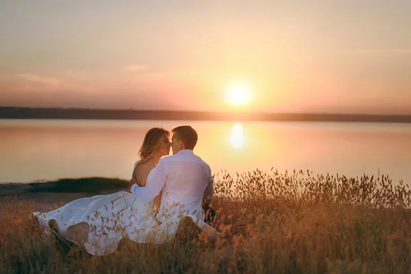 Sposa e sposo camminano insieme al tramonto vicino al mare — Foto Stock