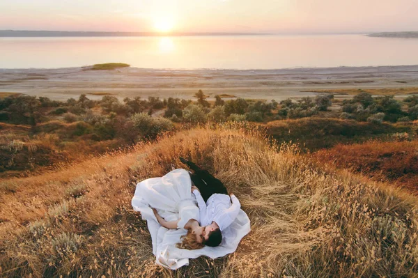 Жених и невеста идут вместе на закате у моря — стоковое фото
