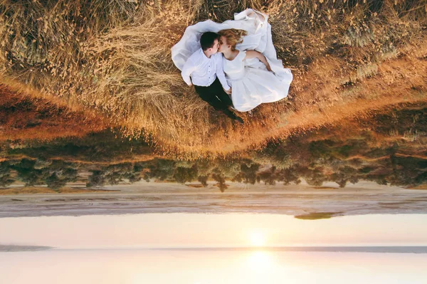 Sposa e sposo camminano insieme al tramonto vicino al mare — Foto Stock