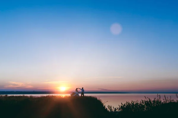 Bruden och brudgummen går ihop vid solnedgången nära havet — Stockfoto