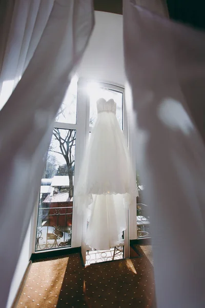 Une belle robe de mariée suspendue dans une pièce inondée de soleil — Photo