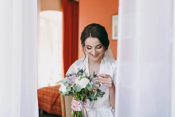 Morena noiva em véu e vestido de cetim branco se senta ao lado da janela — Fotografia de Stock
