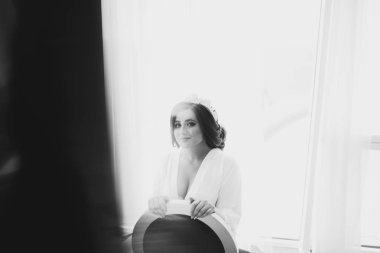 Gelin esmer beyaz saten sabahlık pencerenin kenarında oturur