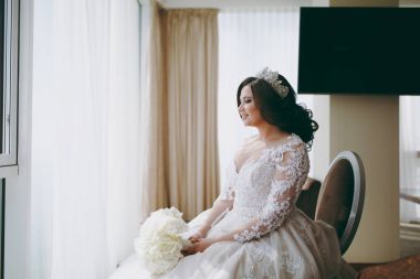 Bir gelinlik güzel gelin pencerenin yanındaki sandalyeye oturur