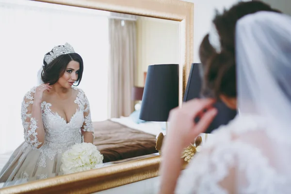 Красивая невеста в свадебном платье в апартаментах стоит у зеркала — стоковое фото