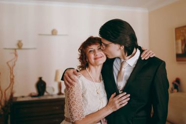 Groom in the suit standing with his mother at home in the morning clipart