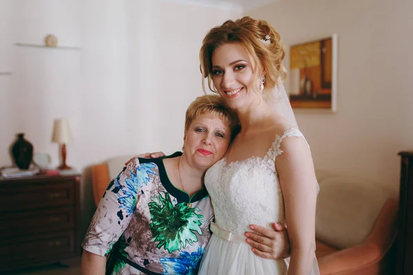 Bride in wedding dress standing with mother at home in the morning — Stock Photo, Image