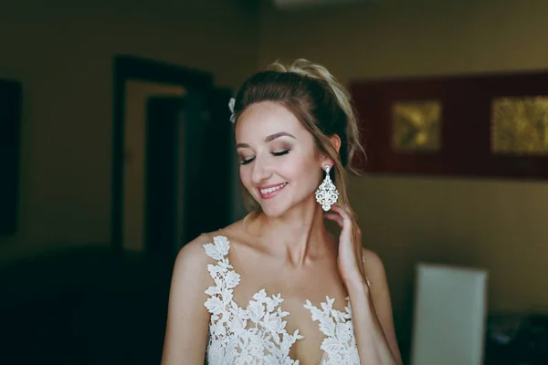 Blonde bride puts on earrings in the morning in the room — Stock Photo, Image
