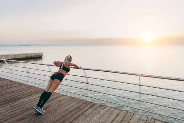 Müzik ve güneş doğarken deniz eğitim Kulaklığımda uzun sarı saçlı genç güzel atletik kız