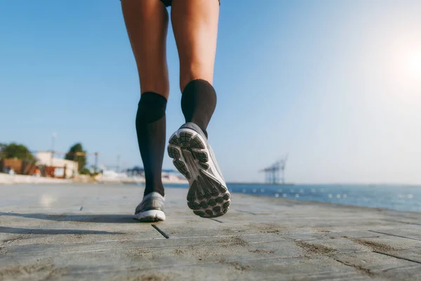 Patas de niña en polainas negras y zapatillas grises, que corre por la mañana al amanecer cerca del mar — Foto de Stock