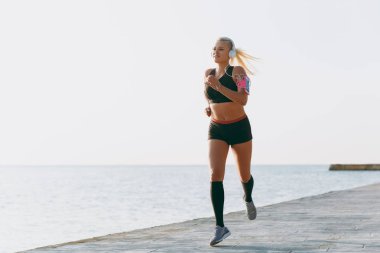 Müzik ve güneş doğarken denizin üzerinde çalışan Kulaklığımda uzun sarı saçlı genç güzel atletik kız