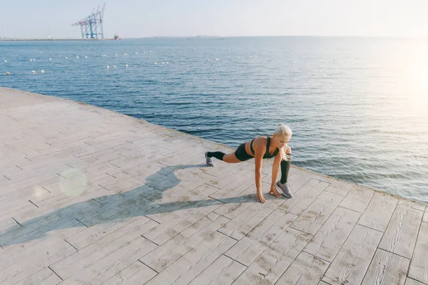 Güneş doğarken denizin üzerinde uzanan yapıyor siyah giysili uzun sarı saçlı genç güzel atletik kız