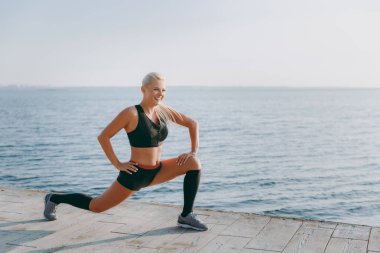 Güneş doğarken denizin üzerinde uzanan yapıyor siyah giysili uzun sarı saçlı genç güzel atletik kız