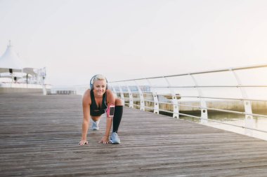 Müzik ve güneş doğarken denizin üzerinde uzanan yapıyor Kulaklığımda uzun sarı saçlı genç güzel atletik kız