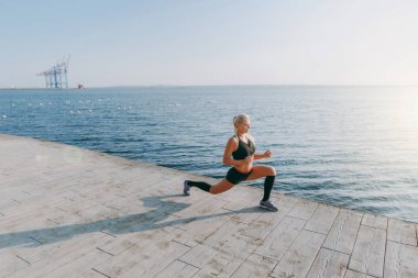 Güneş doğarken denizin üzerinde uzanan yapıyor siyah giysili uzun sarı saçlı genç güzel atletik kız