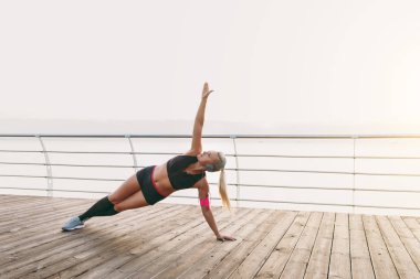 Kulaklığımda uzun sarı saçlı genç güzel atletik kız müzik dinliyor, denizin üzerinde bir el ve gündoğumu eğitim duruyor