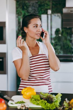 Mutlu kadın mutfakta cep telefonu konuşurken önlük. Sebze salatası. Diyet kavramı. Sağlıklı bir yaşam tarzı. Evde yemek. Yemek hazırlamak.
