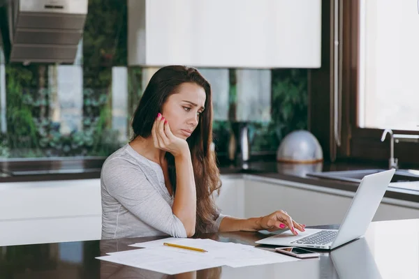 Aantrekkelijke nadenkend en triest zakenvrouw werken met documenten en laptop in de keuken thuis — Stockfoto