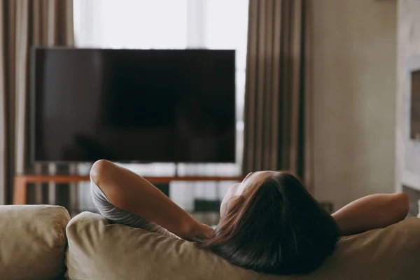 Ung kvinna hemma liggande på soffan, koppla av i hennes vardagsrum och titta på Tv. Stäng upp. Bakifrån. Med plats för text. — Stockfoto